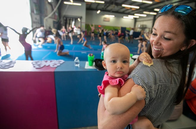 Elliana Rollin, 8 months, enjoys a cookie and her sisters clinic with mom Danielle Rollin as the University of Florida gymnastics team put on a gymnastics clinic at Balance 180 gymnastics Gainesville, FL on Saturday, March 25, 2023. More than 100 young gymnasts learned gymnastics training and routines. They also  met the gymnasts to get autographs and pictures at the NIL Gatorverse event. [Alan Youngblood/Gainesville Sun]
